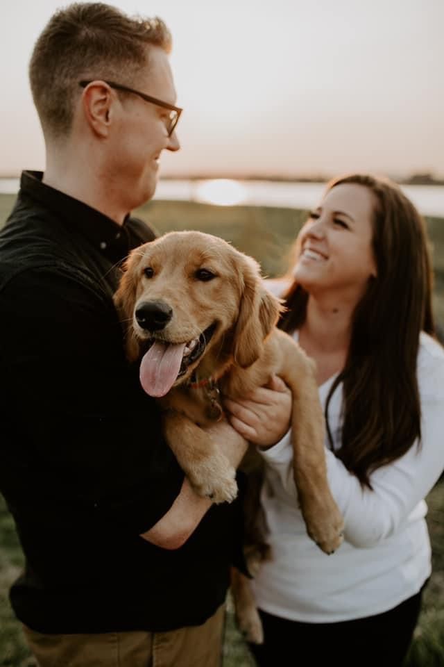 A smiling couple holding their new golden puppy between them